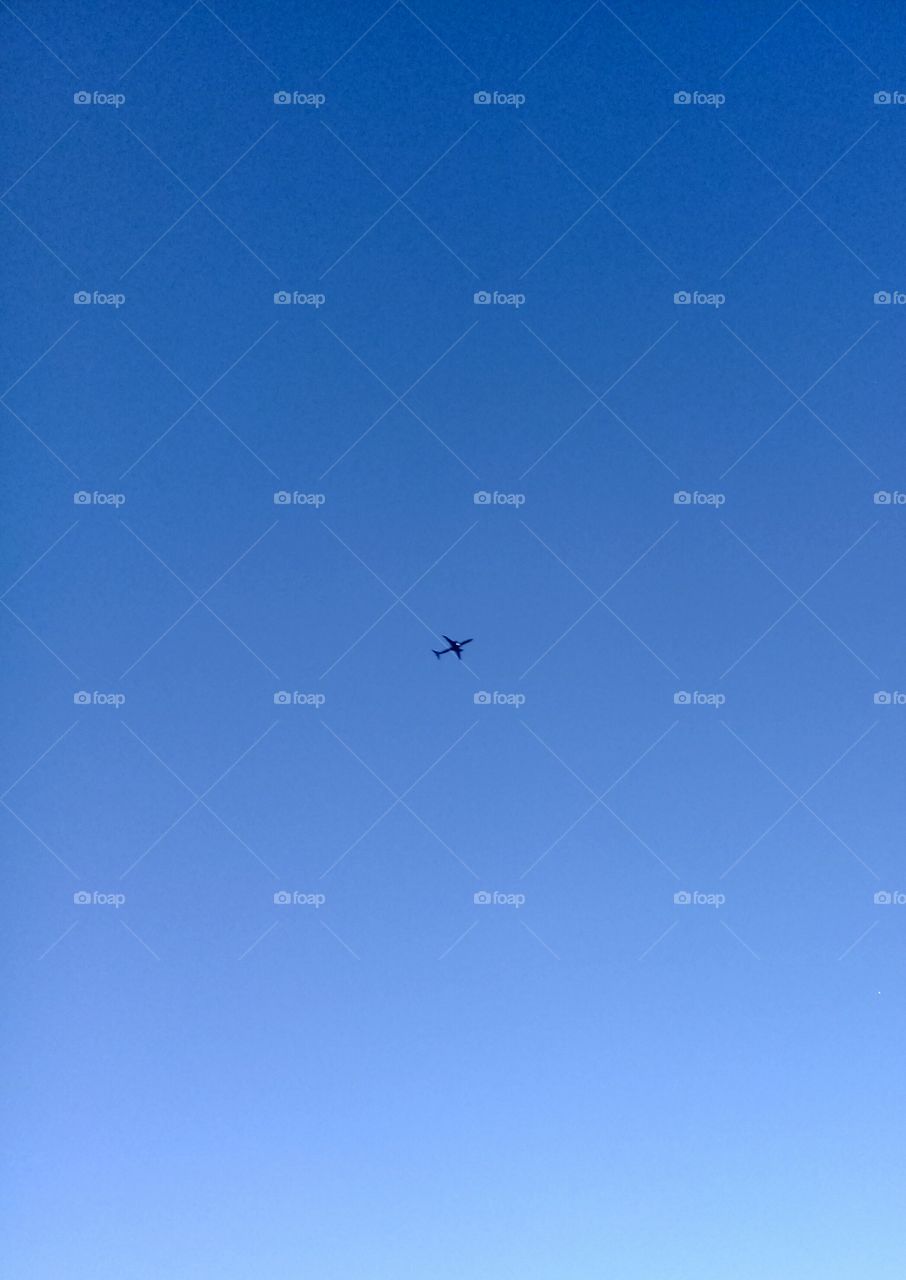 Céu totalmente azul, com um avião ficando diminuto no infinito horizonte.