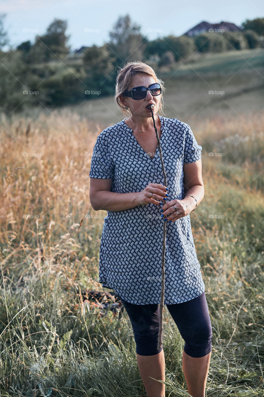 Woman eating marshmallow after roasting it over a campfire on meadow. Vacations close to nature. Candid people, real moments, authentic situations