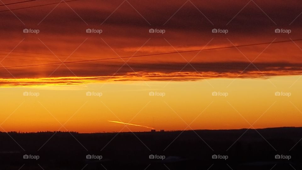red sky sunset over farm in silhouette with a contrail glowing in the sky
