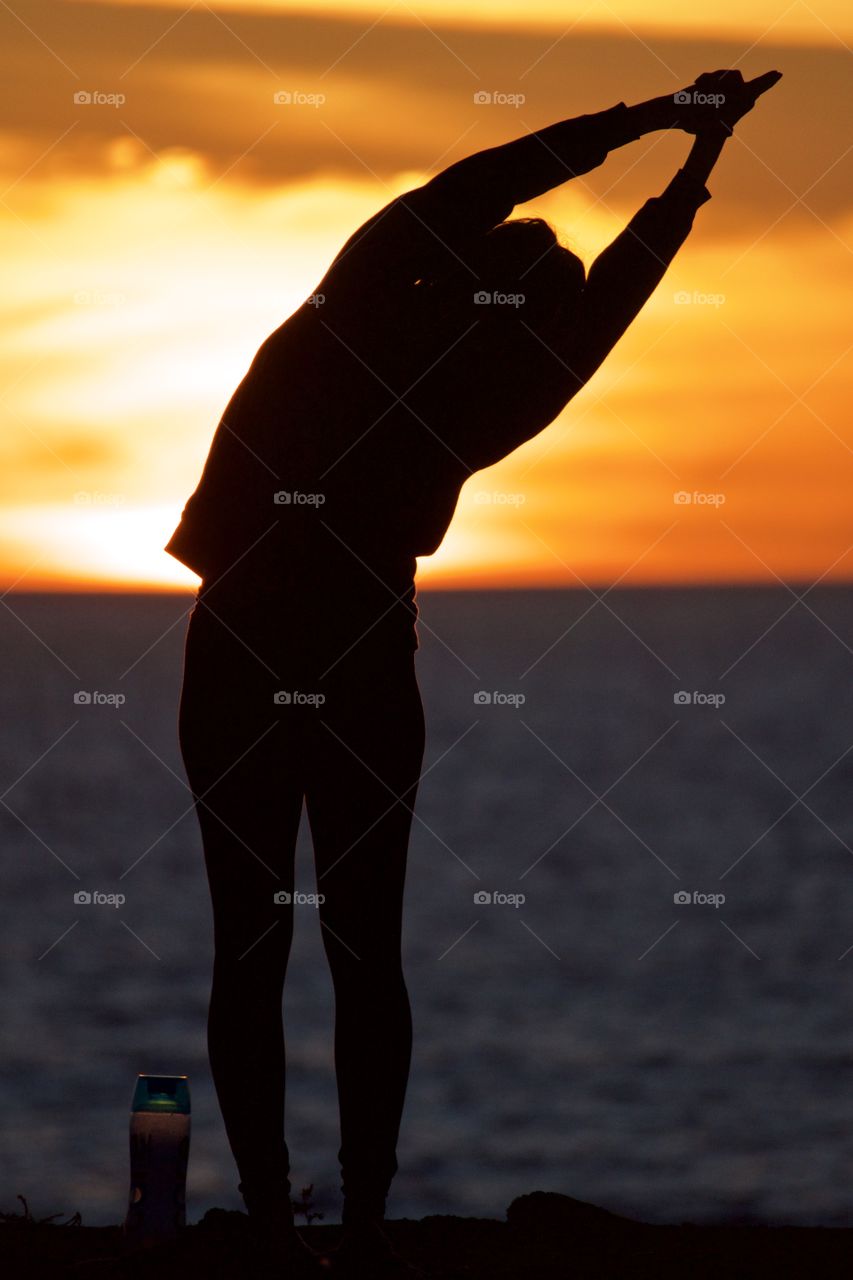 A woman doing yoga on a cliff at sunset 