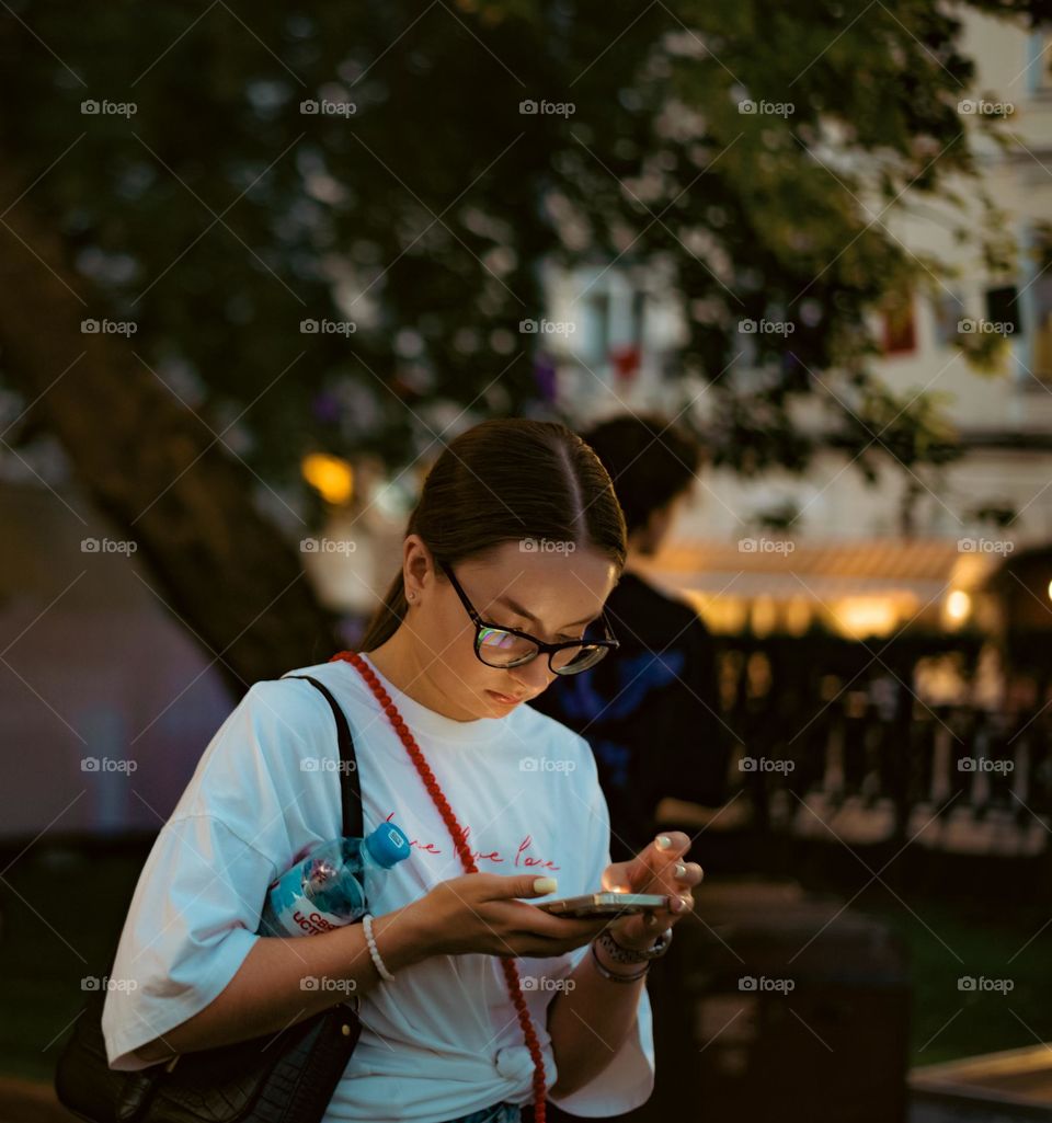 Girl with glasses in the evening looks at the smartphone