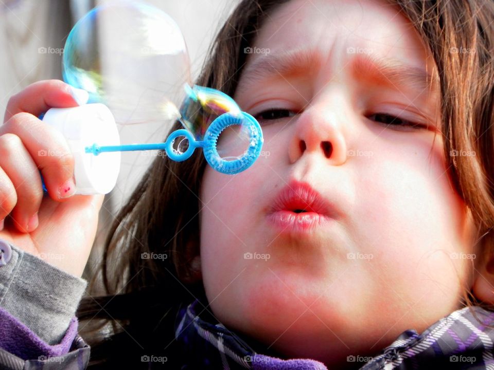 This girls is blowing a bubble outside, she is concentrated and persists on having the biggest bubble she can make