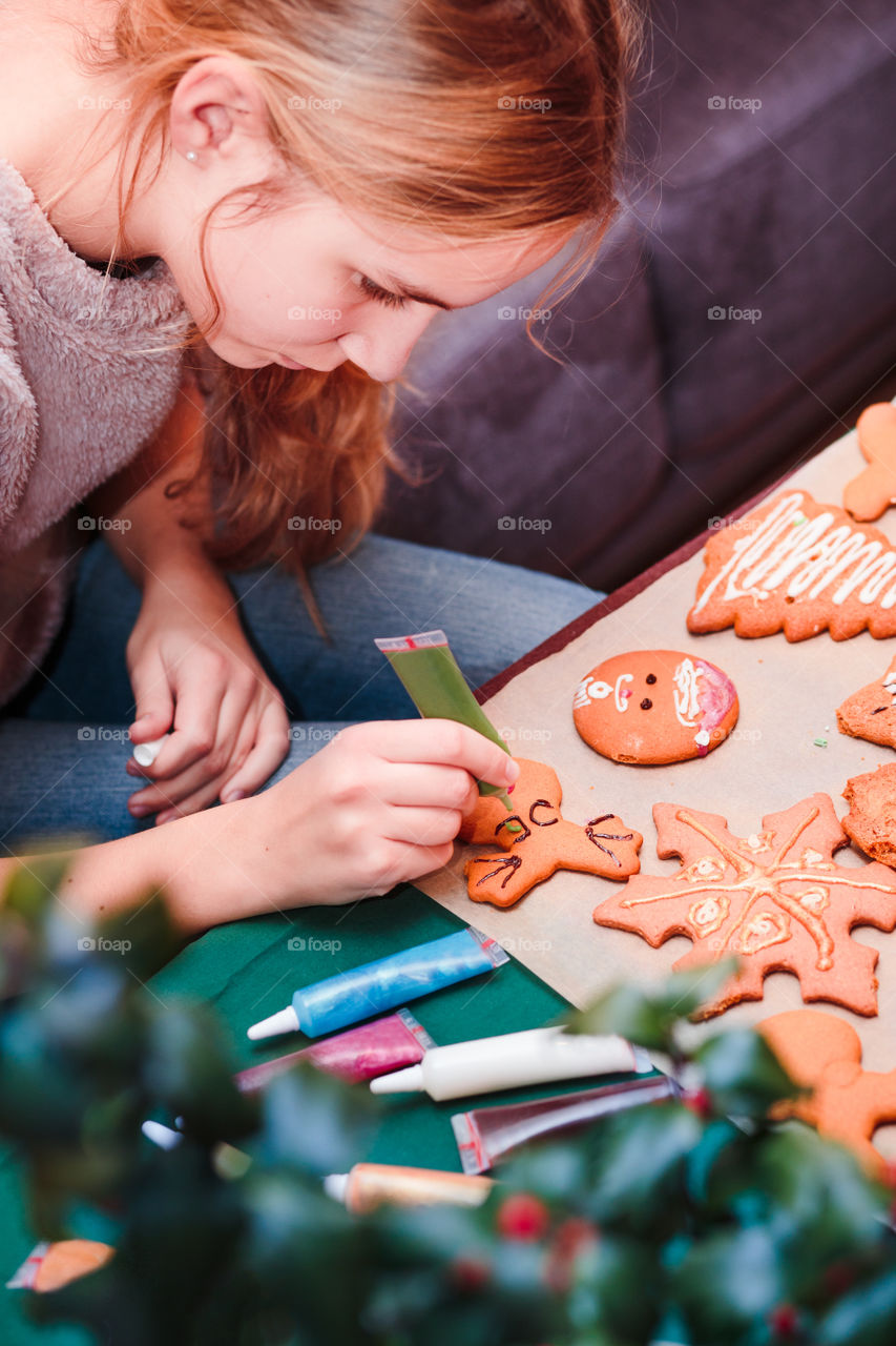 Girl decorating baked Christmas gingerbread cookies with chocolate writing pen