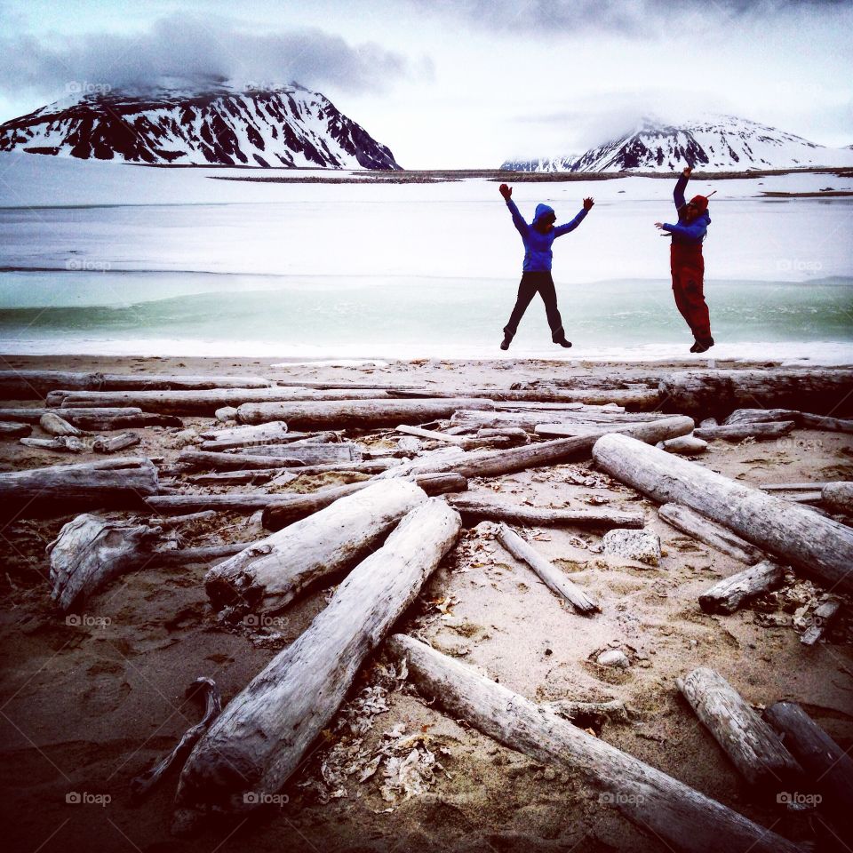 Two people jumping along the shores of a polar beach. Taken at 82 degrees north along the coast of Spitsbergen, Svalbard. 