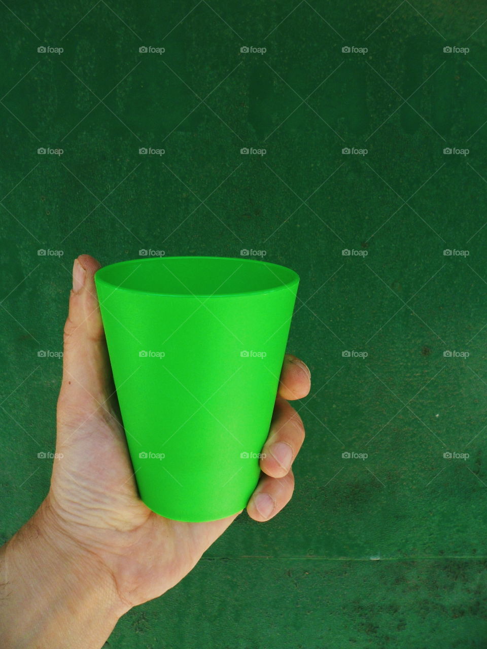 Hand holds a green glass on a green background