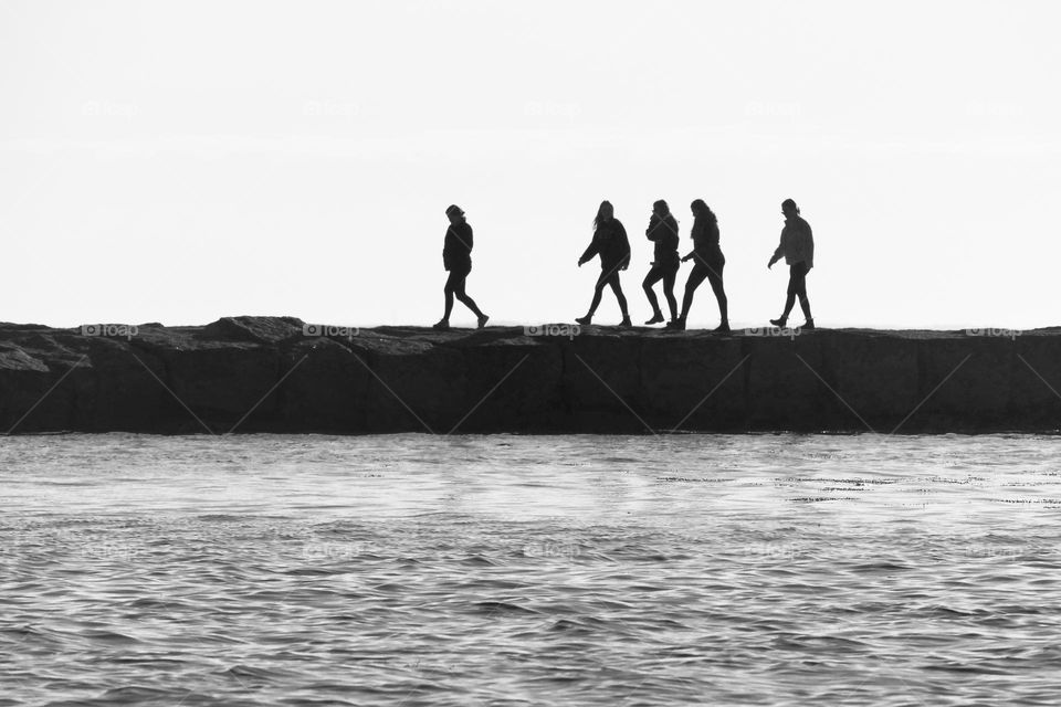 “Breakwater Walkers” A line of silhouettes stroll the stone breakwater on an early, calm morning.