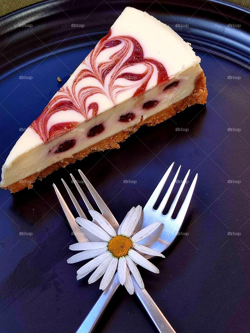 Dessert.  On a black plate is a piece of raspberry brownie.  Nearby are two forks that are crossed.  Chamomile is on the forks