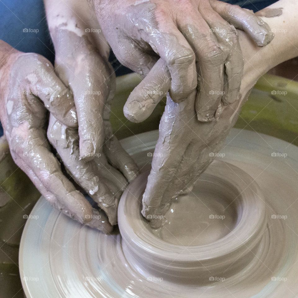 Teaching hands, instructor guiding student’s hands to show how to mold pottery on the pottery  wheel