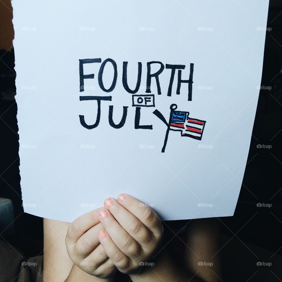 Child holding paper with text Fourth of July american flag