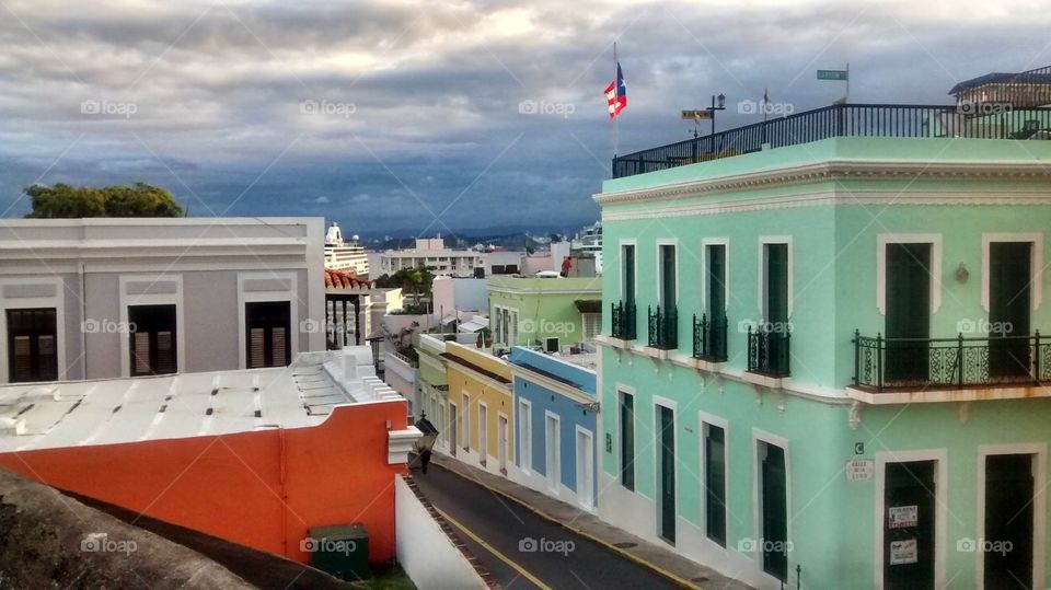 Elevated Shot of Old San Juan, Puerto Rico (Viejo San Juan, Puerto Rico). The dark storm in the mountains and the pastel colored 16th Century Spanish architecture is eye catching and beautiful.