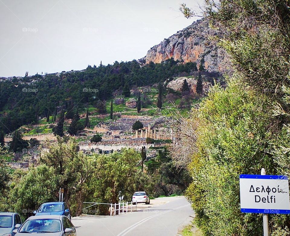 On the road toward Delphi, Greece, with Tholos and Mount Parnassus in background; Delfi street sign