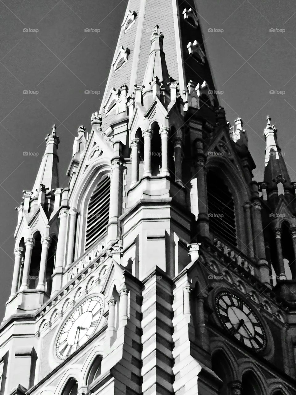 Gothic Cathedral tower with intricate details, columns, clock, arcade, gable, niche, etc. in a black and white photograph.