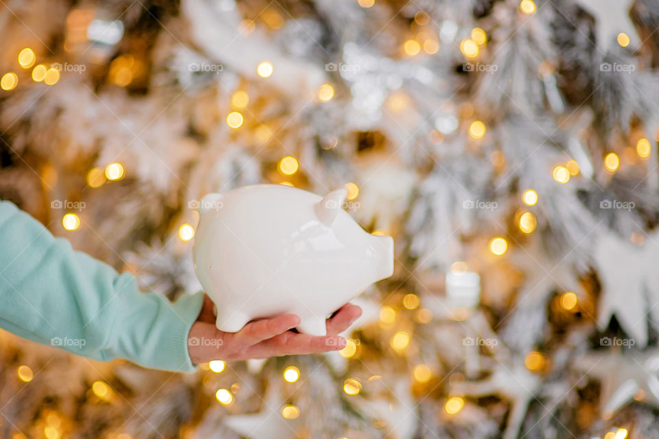 piggy bank with 100 dollars banknote in festive New Year atmosphere of scenery.  Magical bokeh with Christmas tree and bright lights.