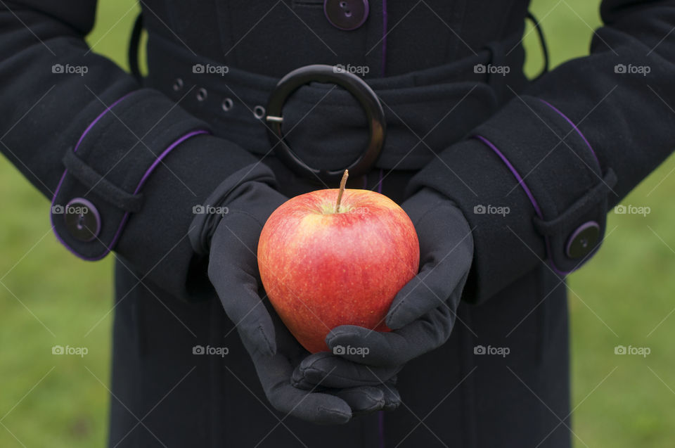 woman in black gloves and a black coat holding a red apple