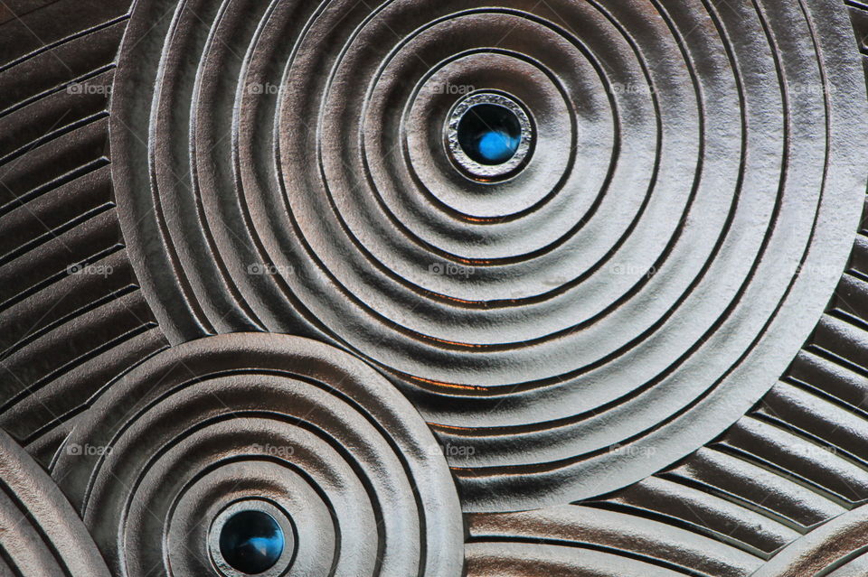 Closeup of a spiral pattern on a glass divider wall creating an abstract that appears silver with blue glass dots in the centre of the spiral.  