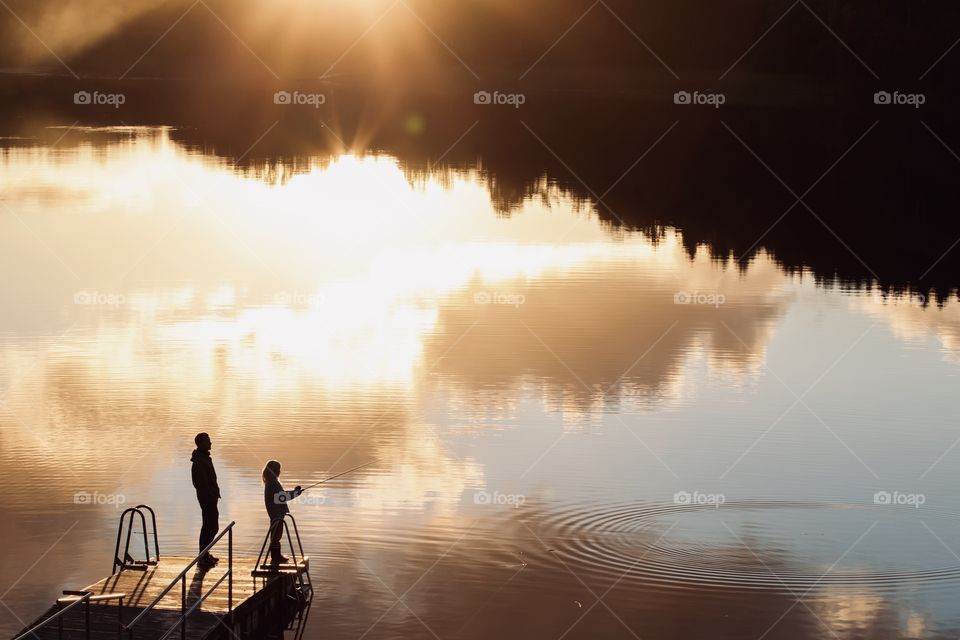 Silhouette of two people fishing in a lake, surrounded by sunlight and reflection in the golden hour 