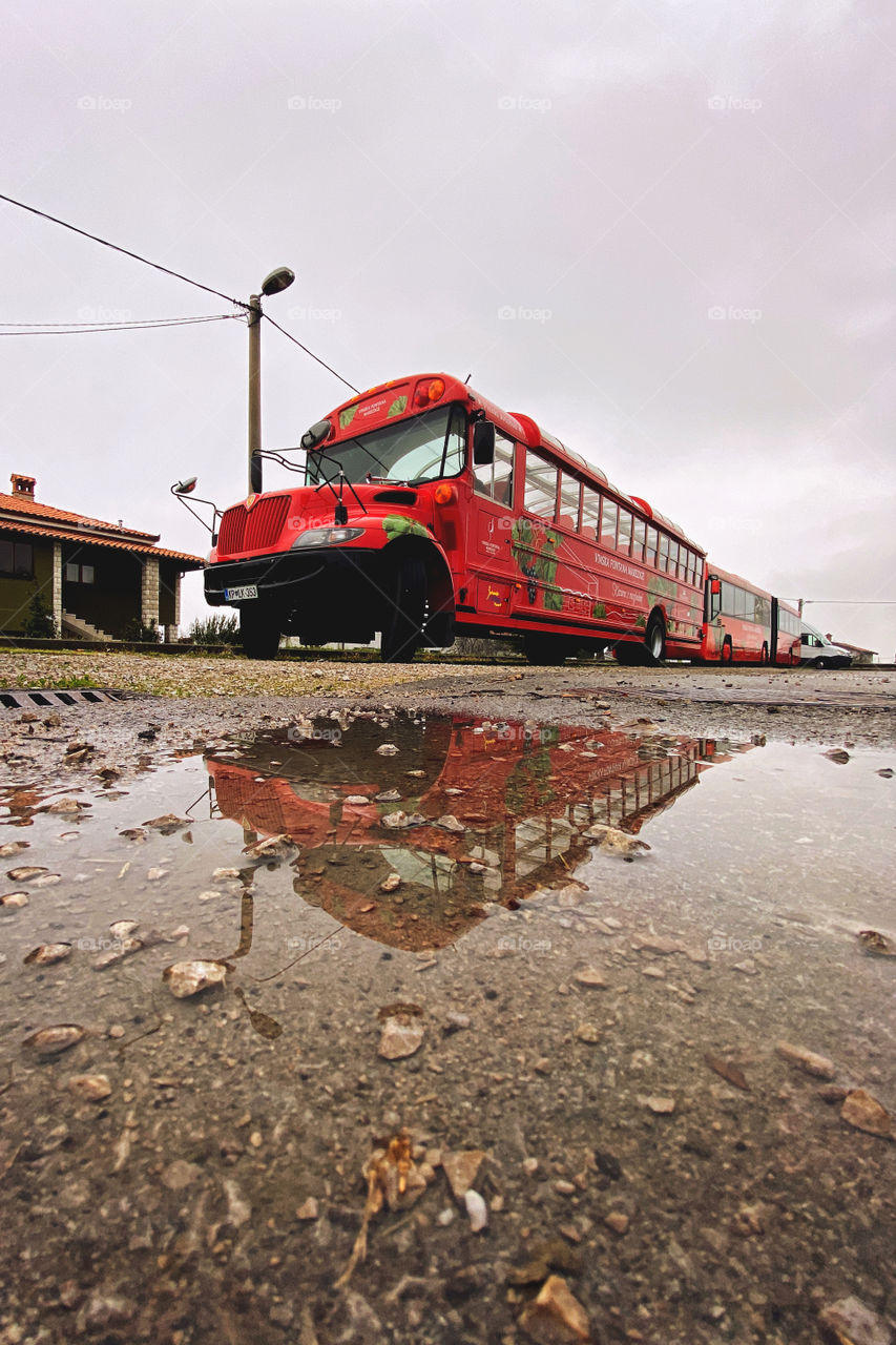 Image of a large red tourist bus reflected in a puddle in winter. Travel conception. Slovenia.