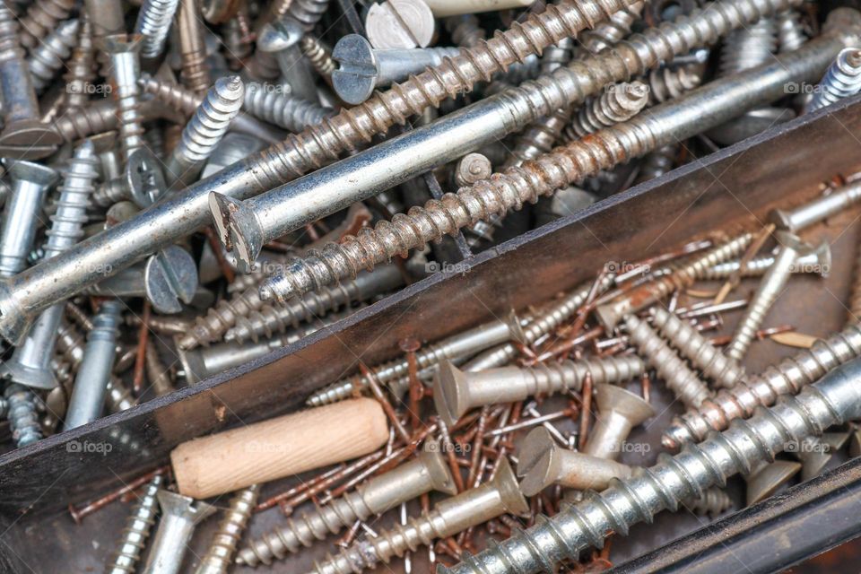 A set of old and new assorted nails, bolts and screws in a plastic organizer box, side view with closeup selective focus. The concept of tools, metal.