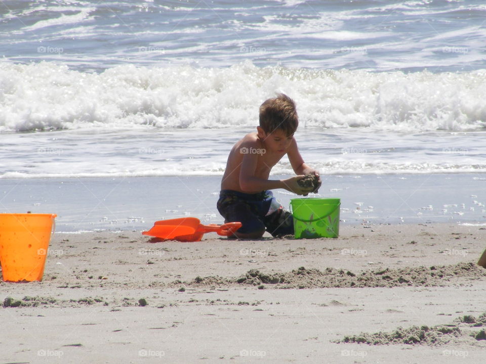 Boy playing in the sand at the beach with a bucket and shovel.