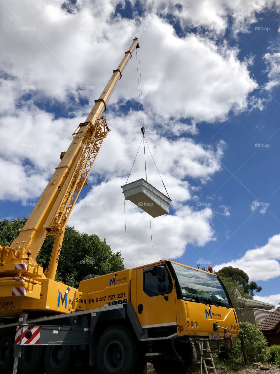 Yellow Giant crane ifting a fibreglass pool over a house