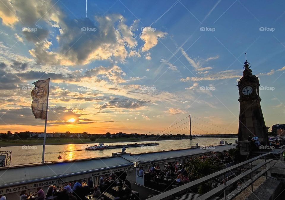 Beautiful cloudy sky on the bring of the sunset in Düsseldorf, Germany/ The setting sun in a blue sky full of clouds and cloudy lines from the passing airplanes/ Phone taken photo of the sunset clouds and the river Rhein