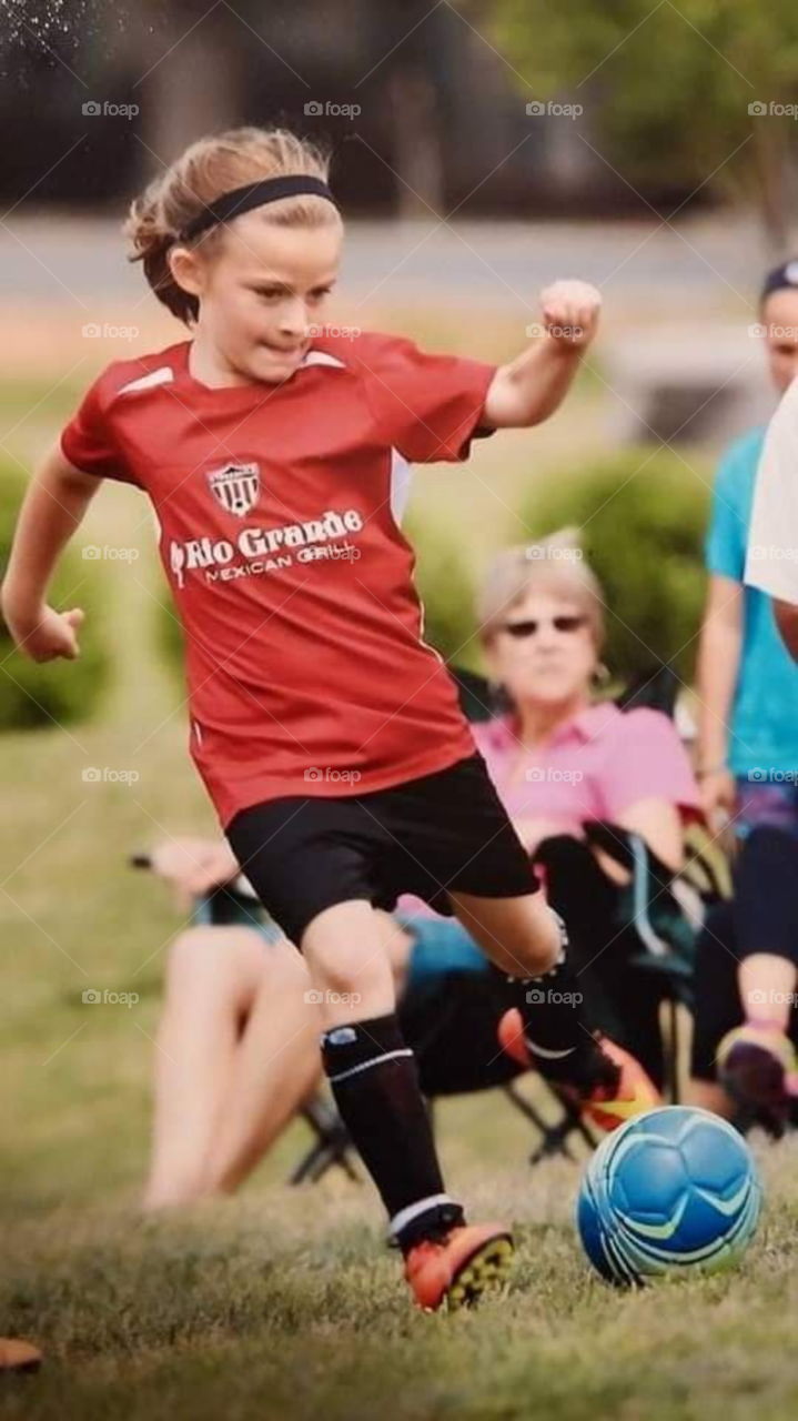 A Young girl in mid kick playing team soccer with onlookers. sport.