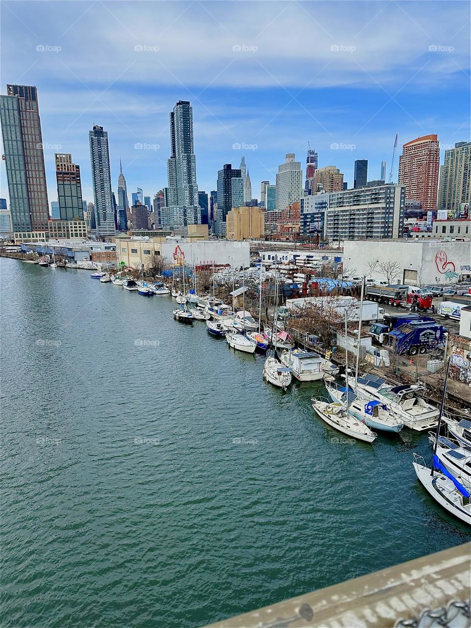 This is „Newtown Creek“ with its many different kinds of boats seen from the „Pulaski Bridge“ that connects „Greenpoint“, Brooklyn to LIC, Queens. In the distance we see „Manhattan“. 2024. Hypnotic Productions
