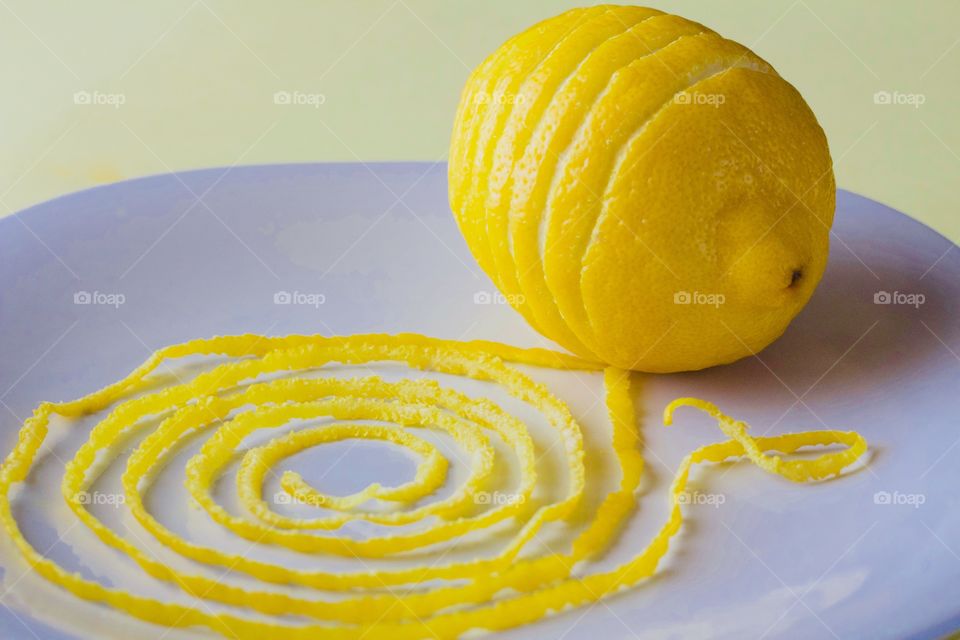 Lemon and spiraled lemon peel on a white plate with yellow background  