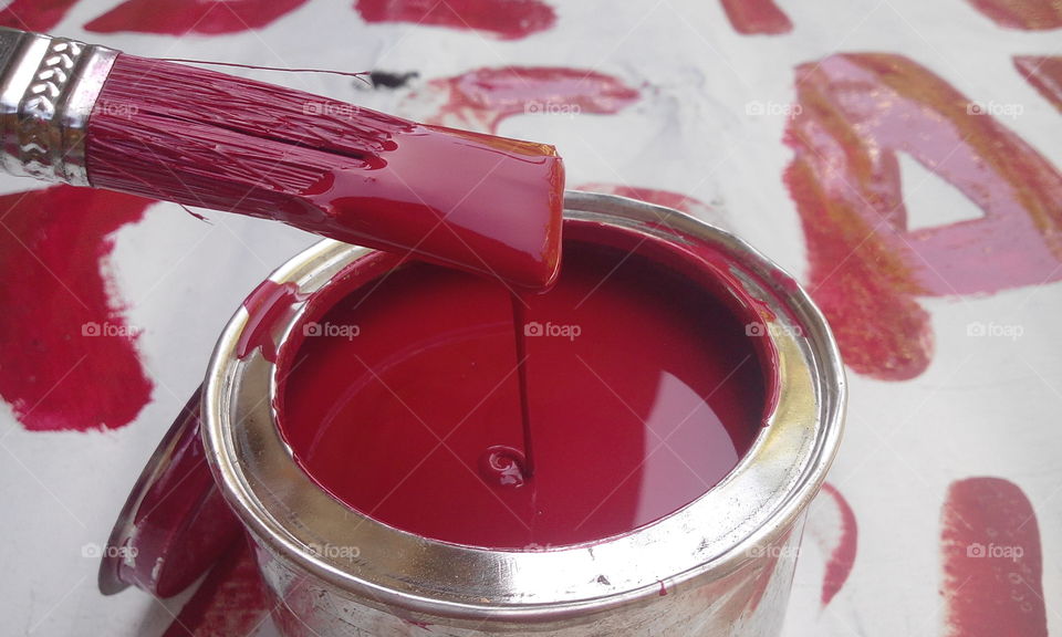 Paintbrush dripping red paint into paint can