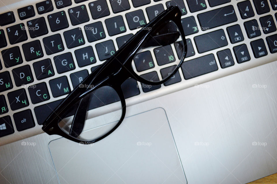 Glasses lie on a black laptop keyboard close-up. A break during work