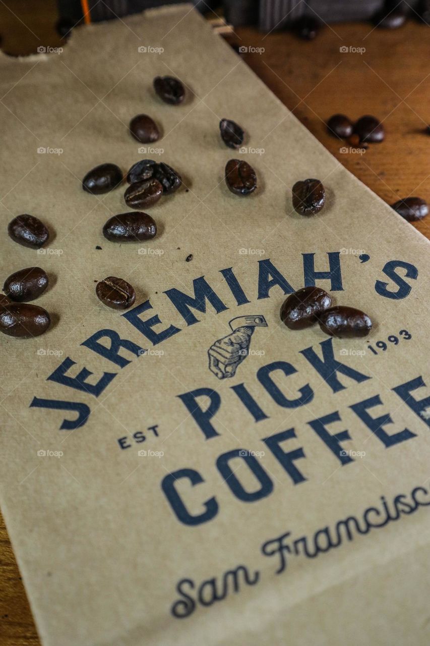 Scattered roasted coffee beans over a bag waiting to be filled with delicious fresh ground coffee beans 