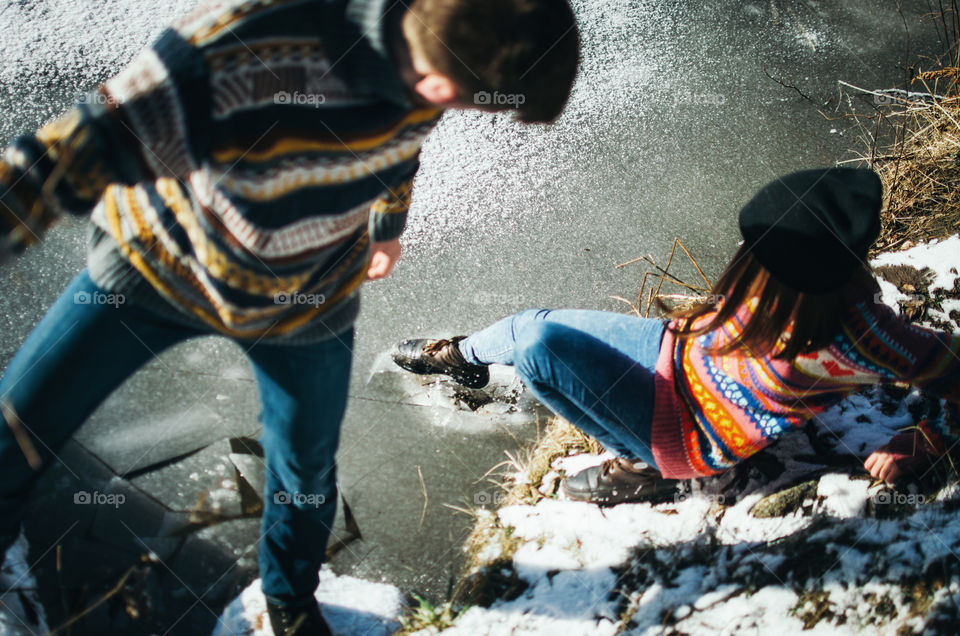 Young woman using a shoe breaks the ice while standing on the shore of a lake. Spring is coming.