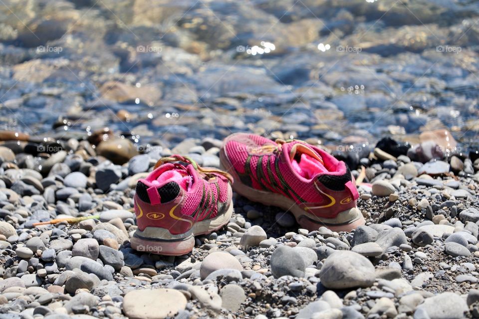 Pair of pink girl's running shoes sneakers on shore beside river