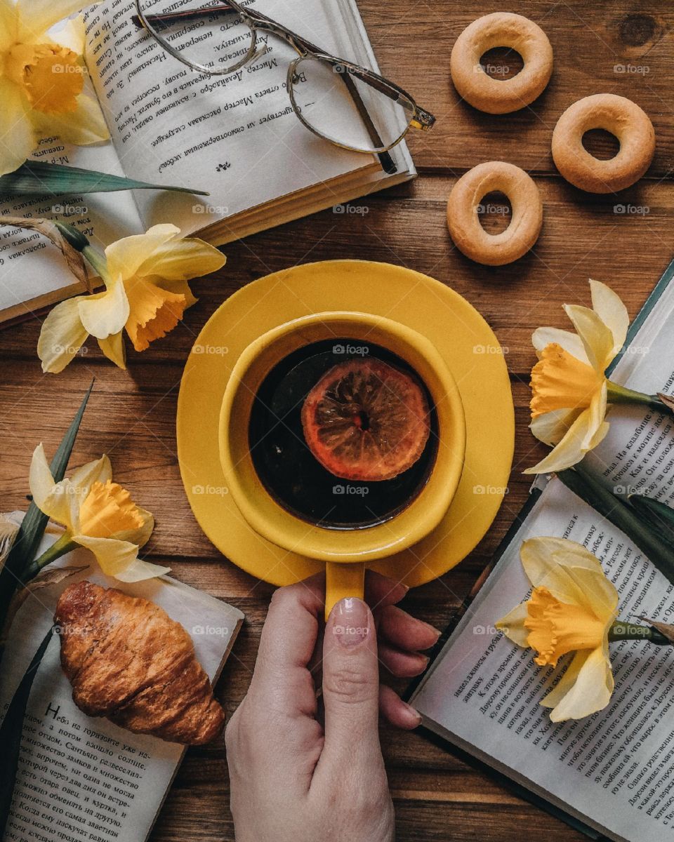 breakfast flat lay with coffee, croissant, books and yellow flowers