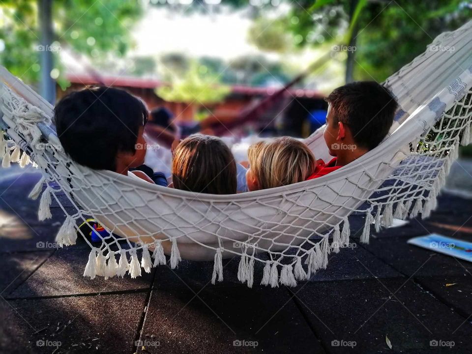 Four youngsters sitting on a white hammock, enjoying the last rays of sun on a beautiful spring afternoon