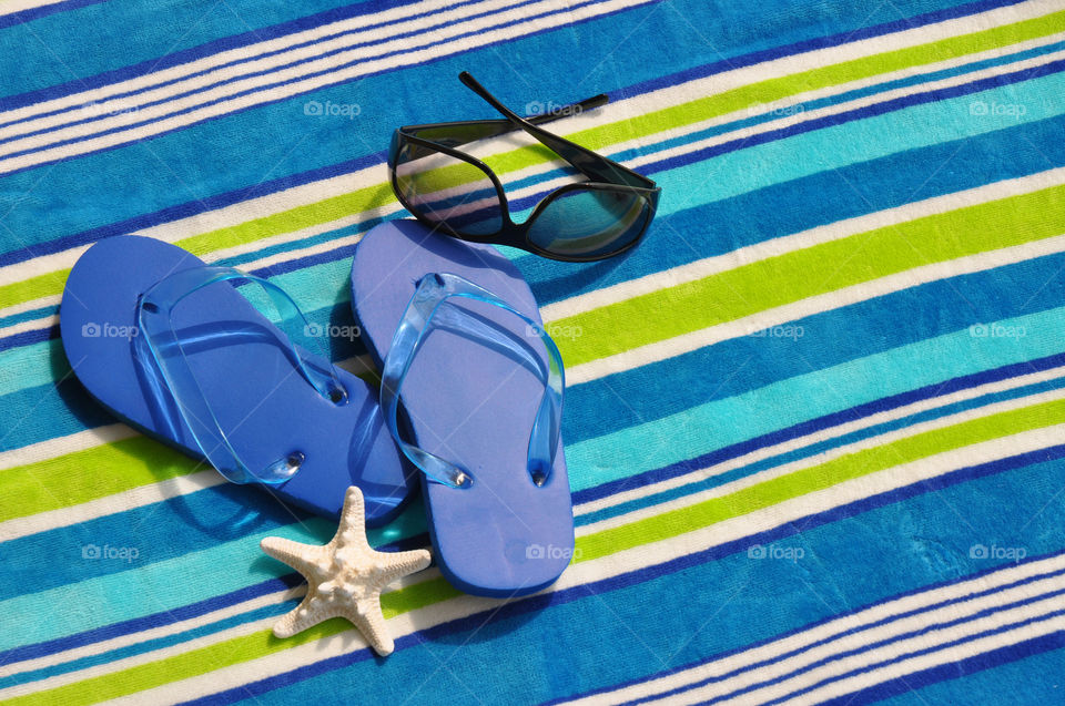 Beach/Summer vacation concept. Flip flops and sunglasses on a striped beach towel. Room for your text. 