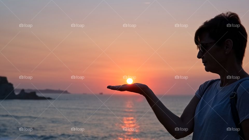 A woman holds the sun on her hand at sunset
