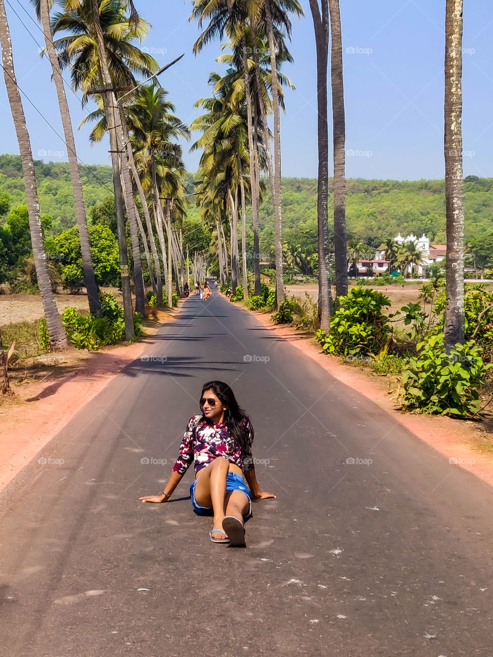 young woman sitting on the middle of the road during her vacation in summer with beautiful palm trees both sides of the road