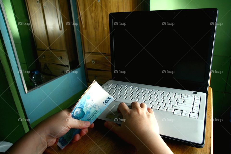 hands holding money while working on a laptop computer