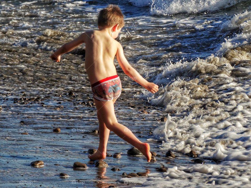 Barefoot Boy Outrunning Ocean Waves. Boy Running From Ocean Waves
