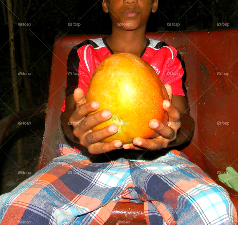 Boy holding a very big and juicy mango