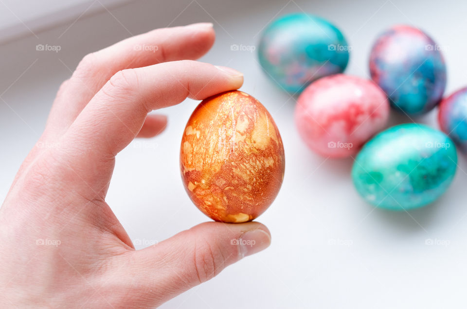 Top view of human hand holding an orange Easter egg on a white background.