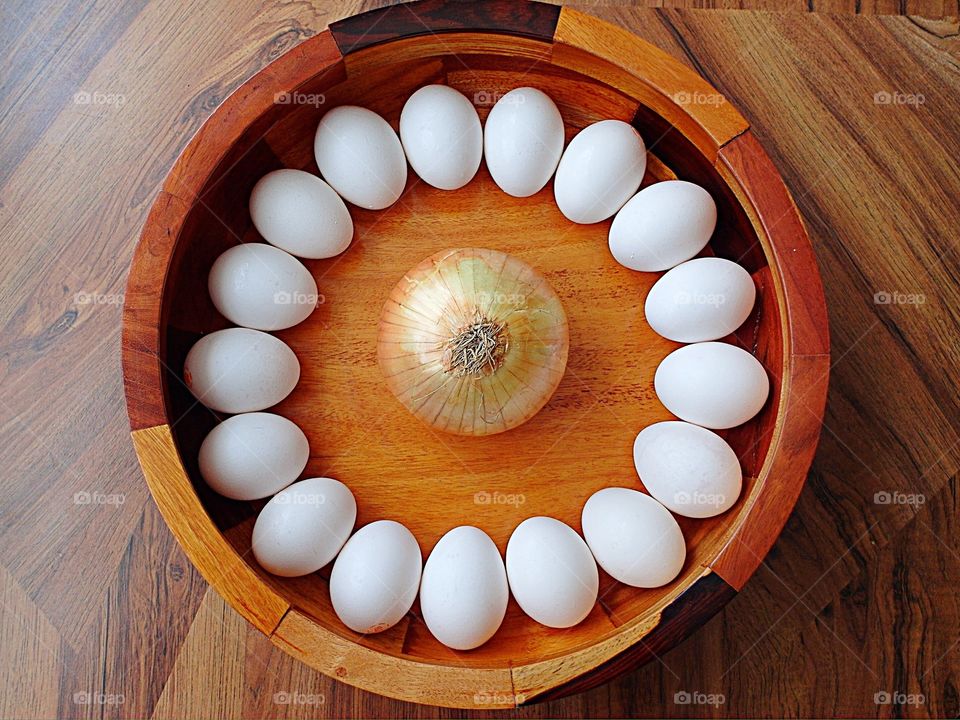 Eggs arranged on a circle around an onion in Woden bowl on a wood table m