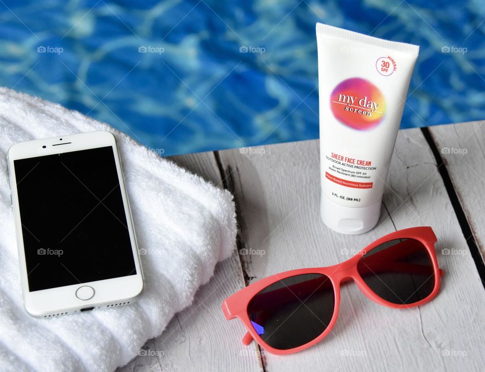 Vacation essentials, sunscreen, sunglasses, phone, towel