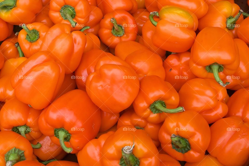 Heap of orange bell peppers with green stems
