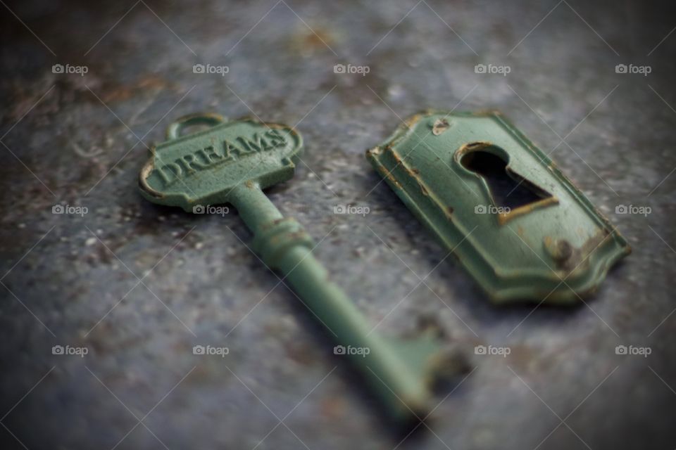 Light teal, metal vintage key with embossed word, “Dreams,” and keyhole on concrete surface 