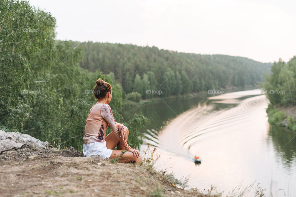 Young slim woman in casual clothes looks at the beautiful view of mountains and calm river, local travel