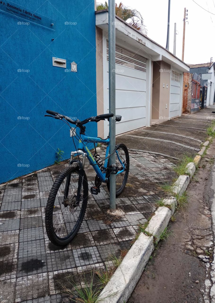 A blue bike locked on a pile on a sidewalk