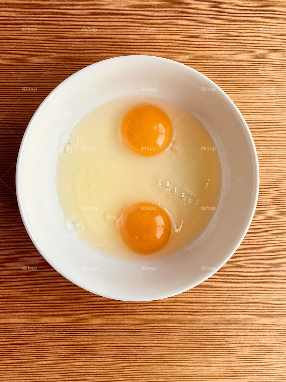 Round eggs yolks inside a round white ceramic bowl seen from above against wooden surface 