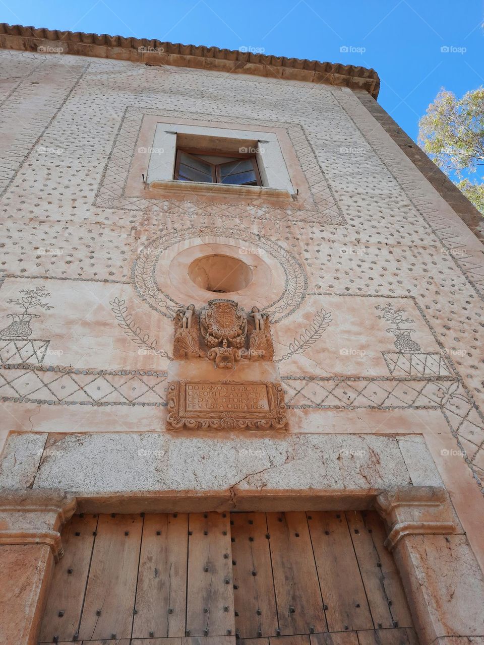 Mediterranean old manor facade. On the wall there is an ancient stone heraldic coat of arms, a window, a rounded window and a  wood door. Majorca, Spain